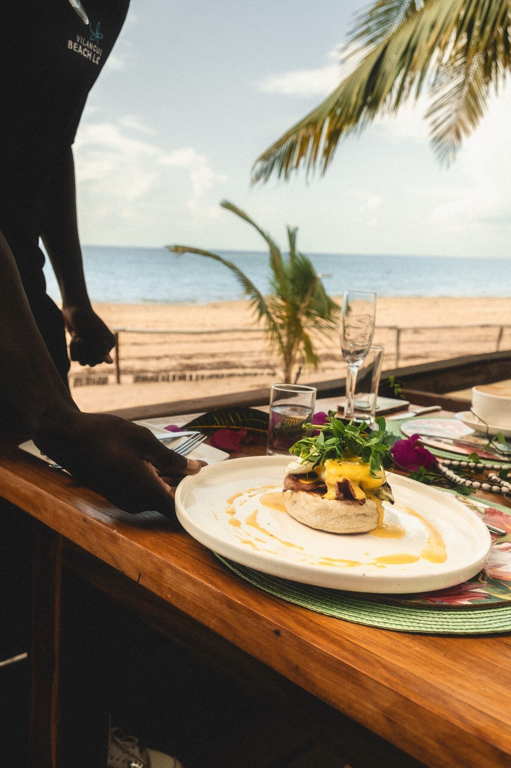 A table with a meal, a glass of water, and a view of the beach.