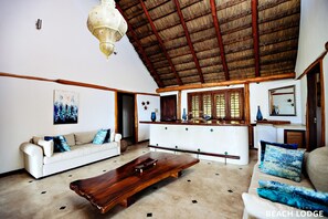 Relax in this spacious living area with a high ceiling, featuring a thatched roof design, a sofa, and a coffee table.