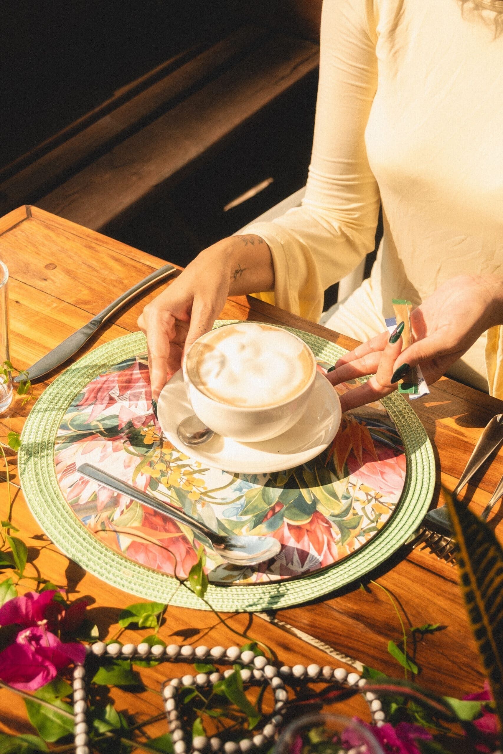 A person holding a cup of coffee on a floral tablecloth.