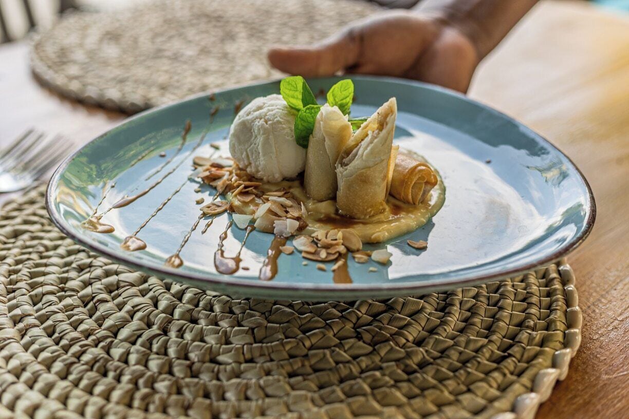 A dessert plate with ice cream, pastry, and nuts on a woven placemat.
