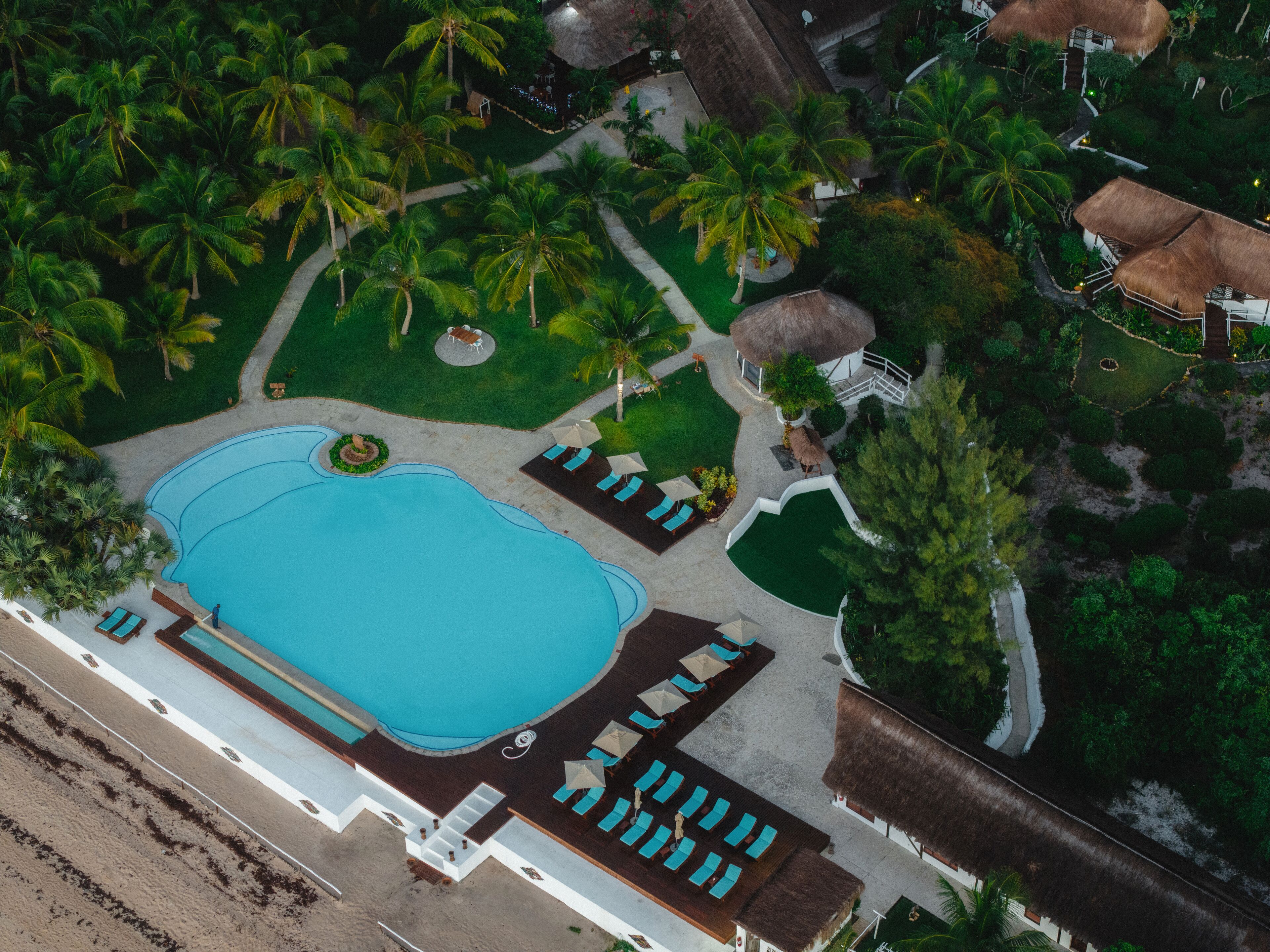 Vista aérea de un resort con una amplia piscina, zonas de descanso y palmeras.