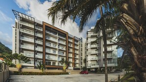 Un edificio residencial de varios pisos con balcones, una zona de estacionamiento y palmeras.