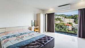 A modern bedroom with a large bed, a desk, and a balcony with a view of buildings and greenery. - Condo in Karon in Chic Condo - Unit B603 (Karon)