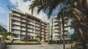 A multi-story residential building with balconies, a parking area, and palm trees.