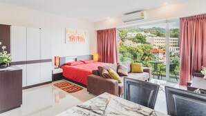 A modern hotel room with a large bed, a sofa, a dining table, and a balcony with a view of the city.