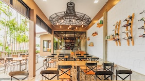 A restaurant with wooden tables and chairs, a large chandelier, and wine racks on the wall.