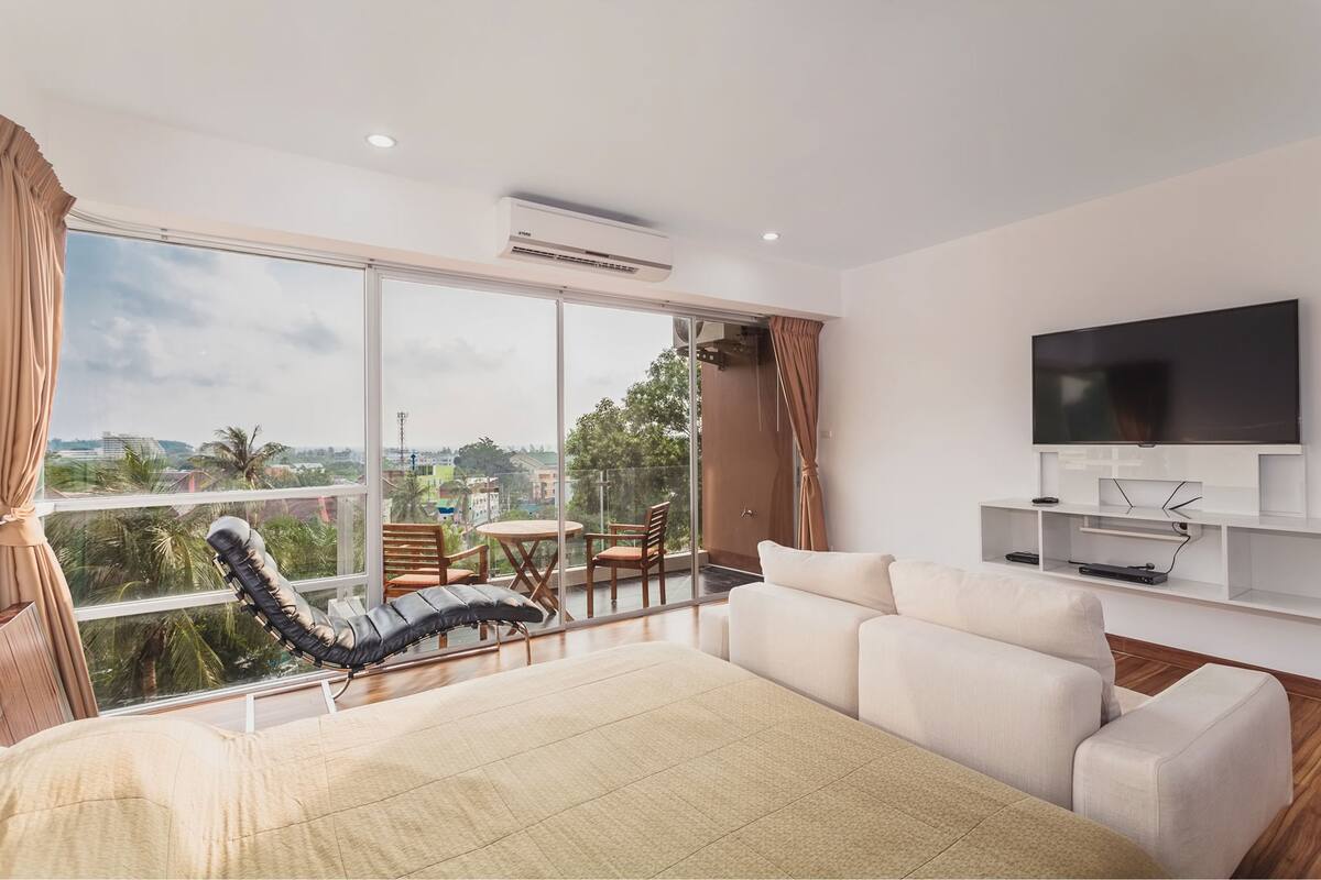 A modern living room with a large window, a sofa, a chair, and a TV mounted on the wall.