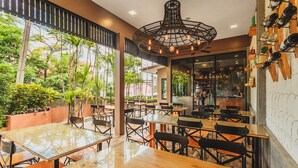 An indoor dining area with glass tables and chairs, a hanging light fixture, and a view of greenery outside. - Condo in Karon in Chic Condo - Unit B708 (Karon)