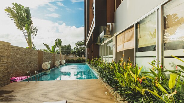 A modern outdoor pool area with a wooden deck, lounge chairs, and tropical plants. - Condo in Karon in Chic Condo - Unit B708 (Karon)