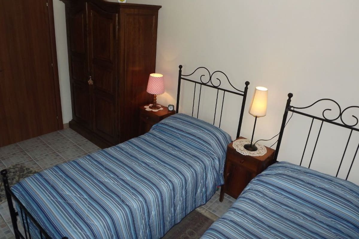 A bedroom with two beds, wooden wardrobe, and bedside lamps.