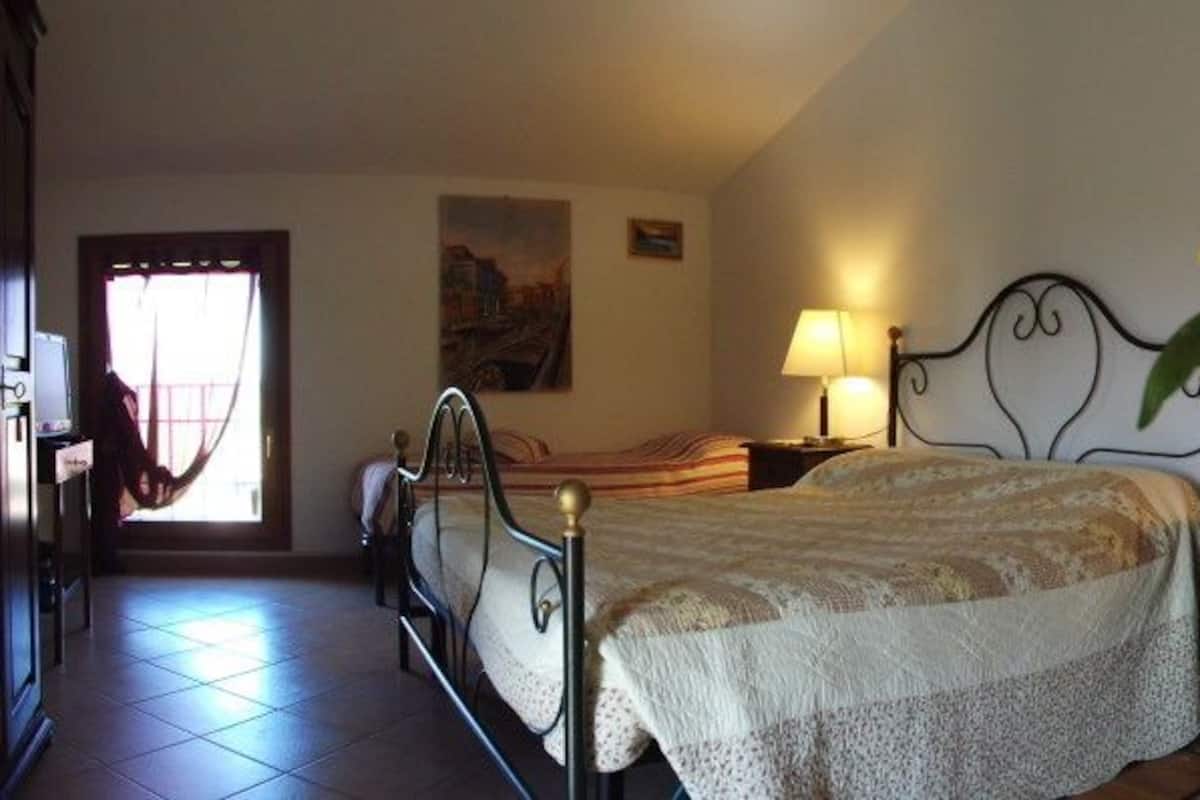 A bedroom with a bed, bedside table, lamp, and a potted plant with yellow flowers.
