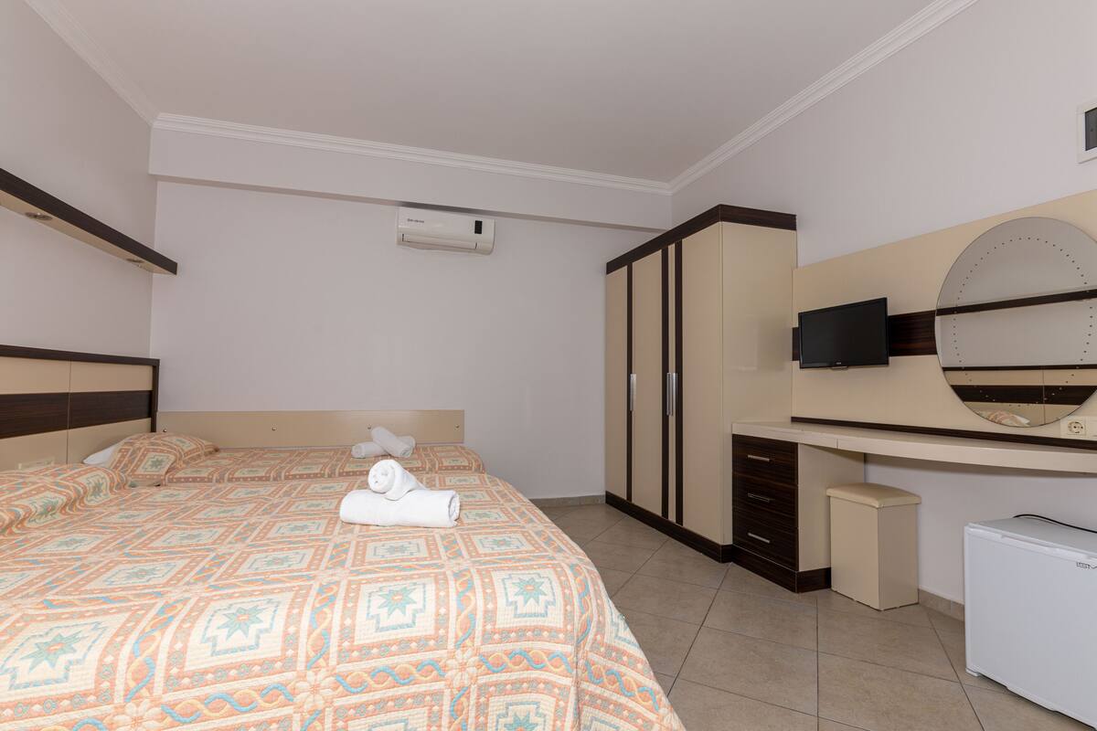 A hotel room with a large bed, a TV, a wardrobe, and a small refrigerator.