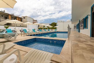 Una piscina al aire libre, sombrillas, sillones reclinables de piscina