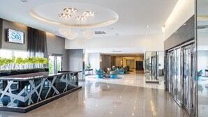 A spacious lobby with a modern chandelier, seating area, and a reception desk. - Withus Condotel at Sea Residences (Pasay)