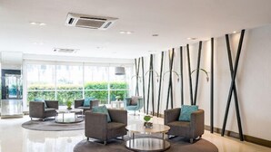 A modern lobby with grey sofas, round coffee tables, and a large window offering a view of greenery. - Withus Condotel at Sea Residences (Pasay)