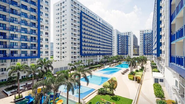 A high-rise hotel with multiple balconies, a central swimming pool, and surrounding greenery. - Withus Condotel at Sea Residences (Pasay)