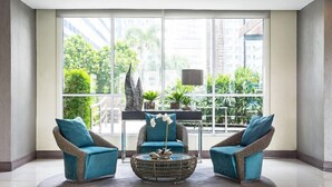 A spacious room with large windows, wicker chairs, a round coffee table, and a view of greenery and buildings. - Withus Condotel at Sea Residences (Pasay)