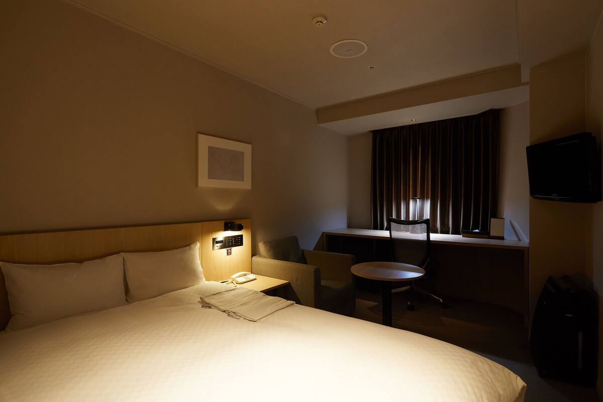 Een hotelkamer met een groot bed, een bureau met stoel, een televisie en een raam met gordijnen.