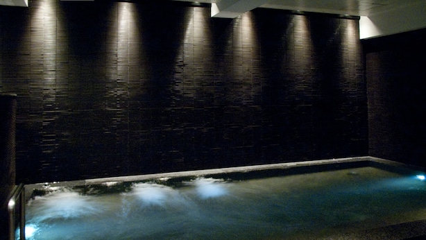 A spa area with a heated floor, dark tiled walls, and a reflective water surface. - Rhino Hotel Kyoto (Kyoto)