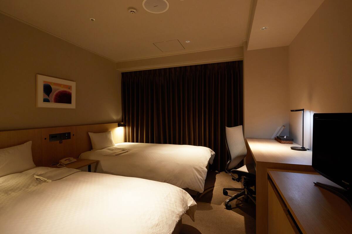 Een hotelkamer met twee bedden, een bureau met een computer, een televisie en een gordijn.