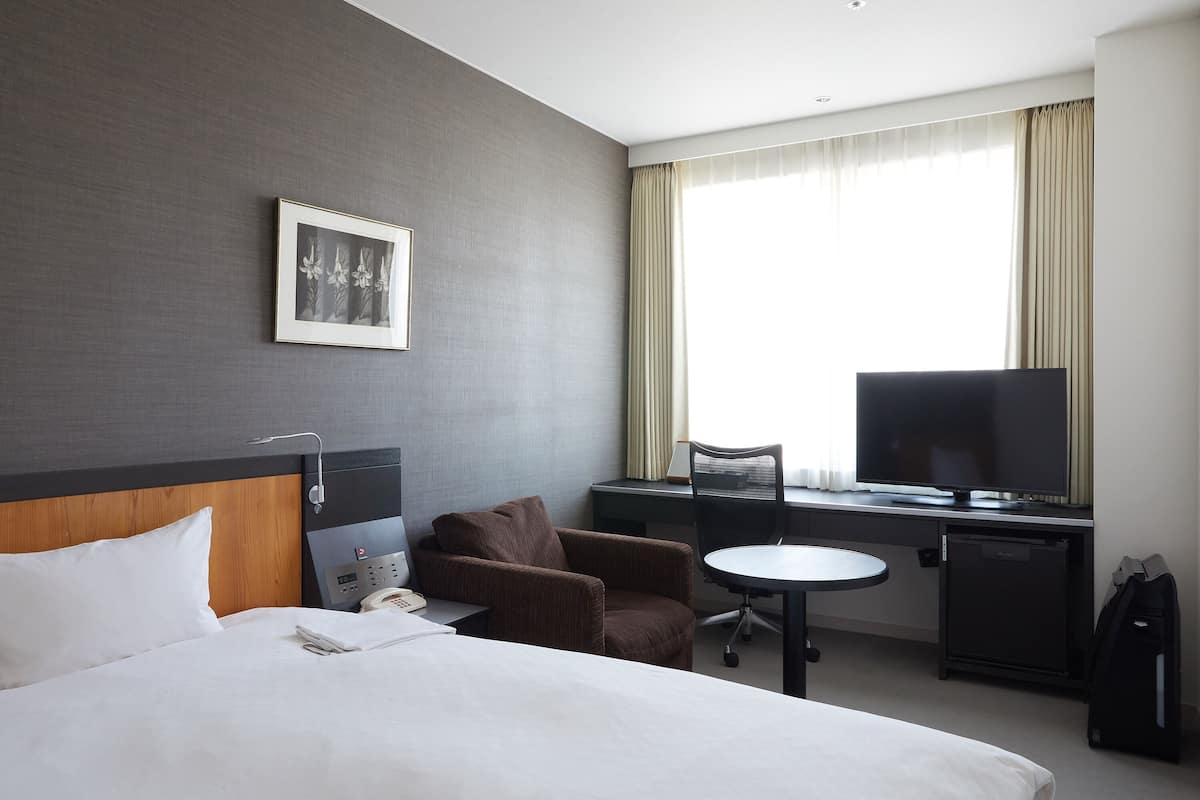 Een hotelkamer met een bed, een bureau met stoel, een televisie en een klein kastje.
