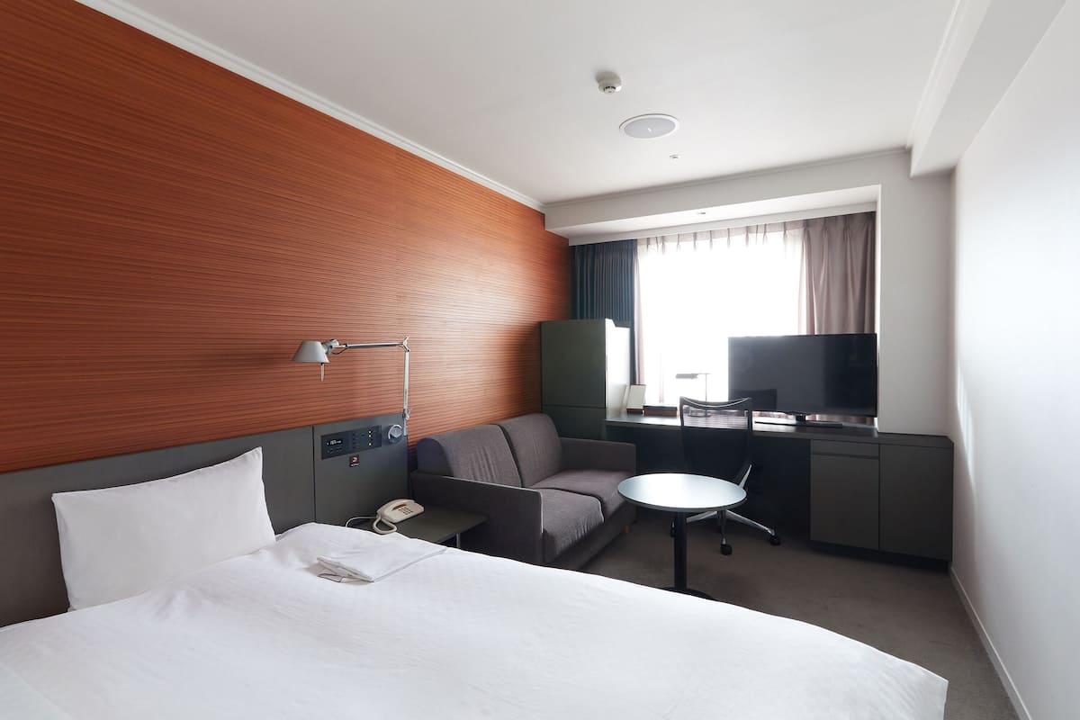 Een hotelkamer met een bed, een slaapbank, een bureau, een stoel, een televisie en een raam met gordijnen.