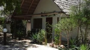 A house with a thatched roof, surrounded by lush greenery and a stone pathway. - Caliente Beach Lodge (Toliara)