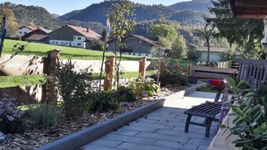 Un sendero pavimentado que lleva a un banco de madera, con un edificio rústico y un paisaje montañoso al fondo.