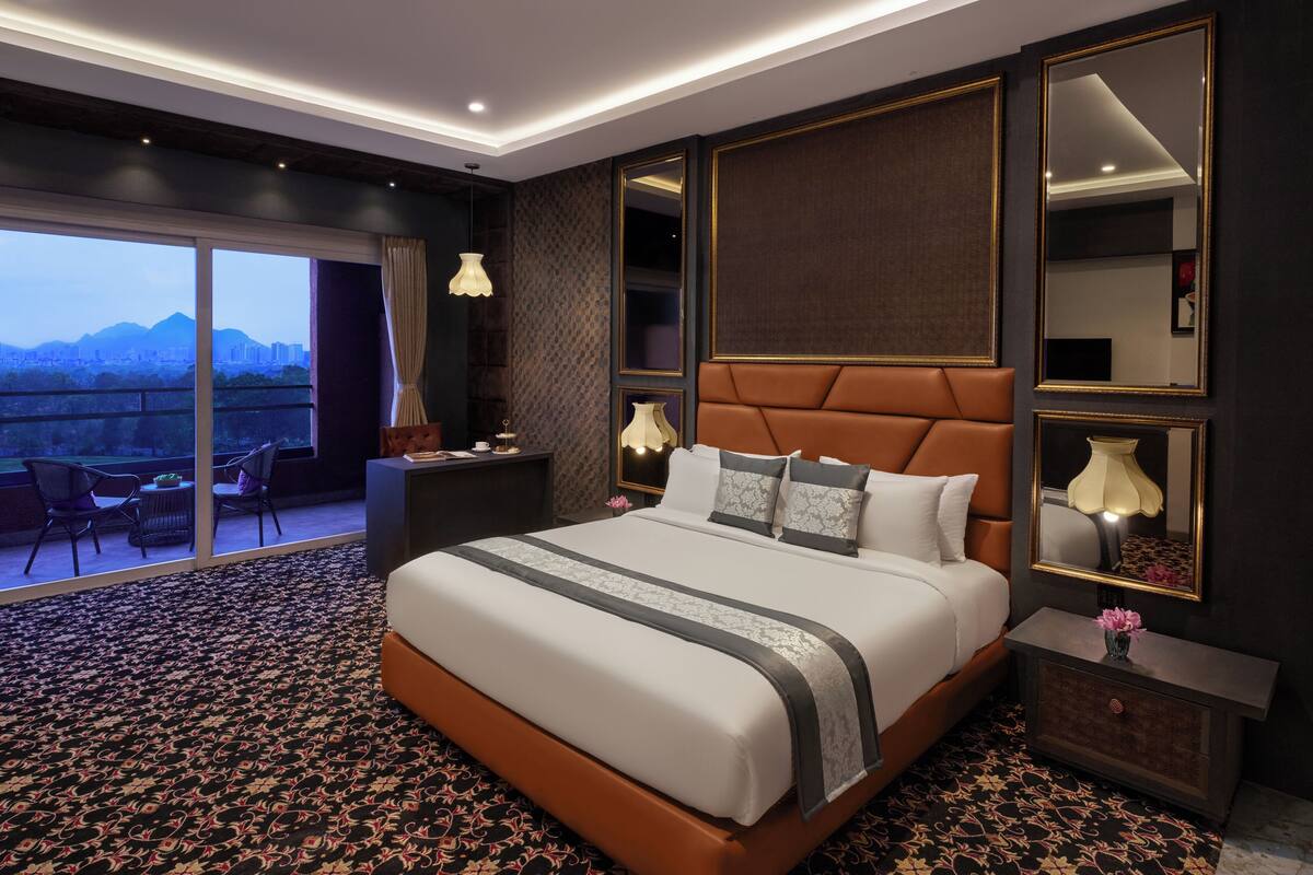 A spacious hotel room with a large bed, a balcony with a city view, and a modern design.