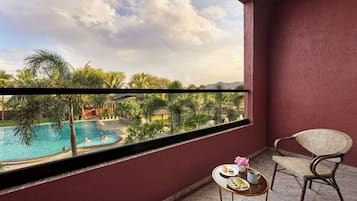 Ein Balkon mit Blick auf einen Swimmingpool, umgeben von Palmen und einem Berg im Hintergrund.