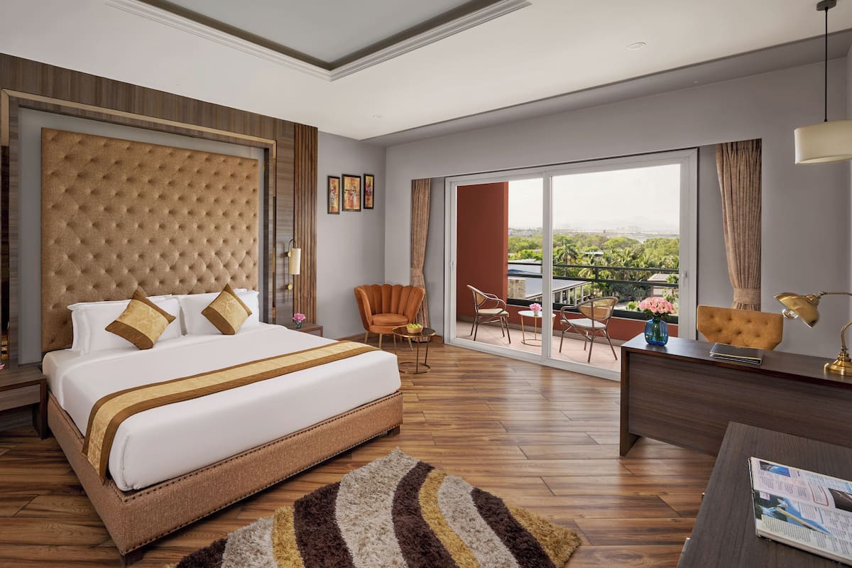 A modern hotel room with a large bed, a balcony with a view, and a desk with a lamp.