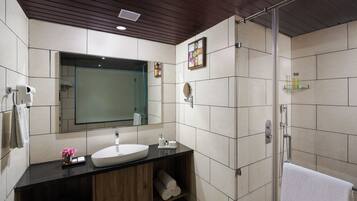 Et moderne badeværelse med træloft, stort spejl, hvid vask og brusekabine i glas.