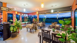 A restaurant with indoor dining tables and chairs, potted plants, and a view of the outdoors. - Samsha Guesthouse (Hua Hin)
