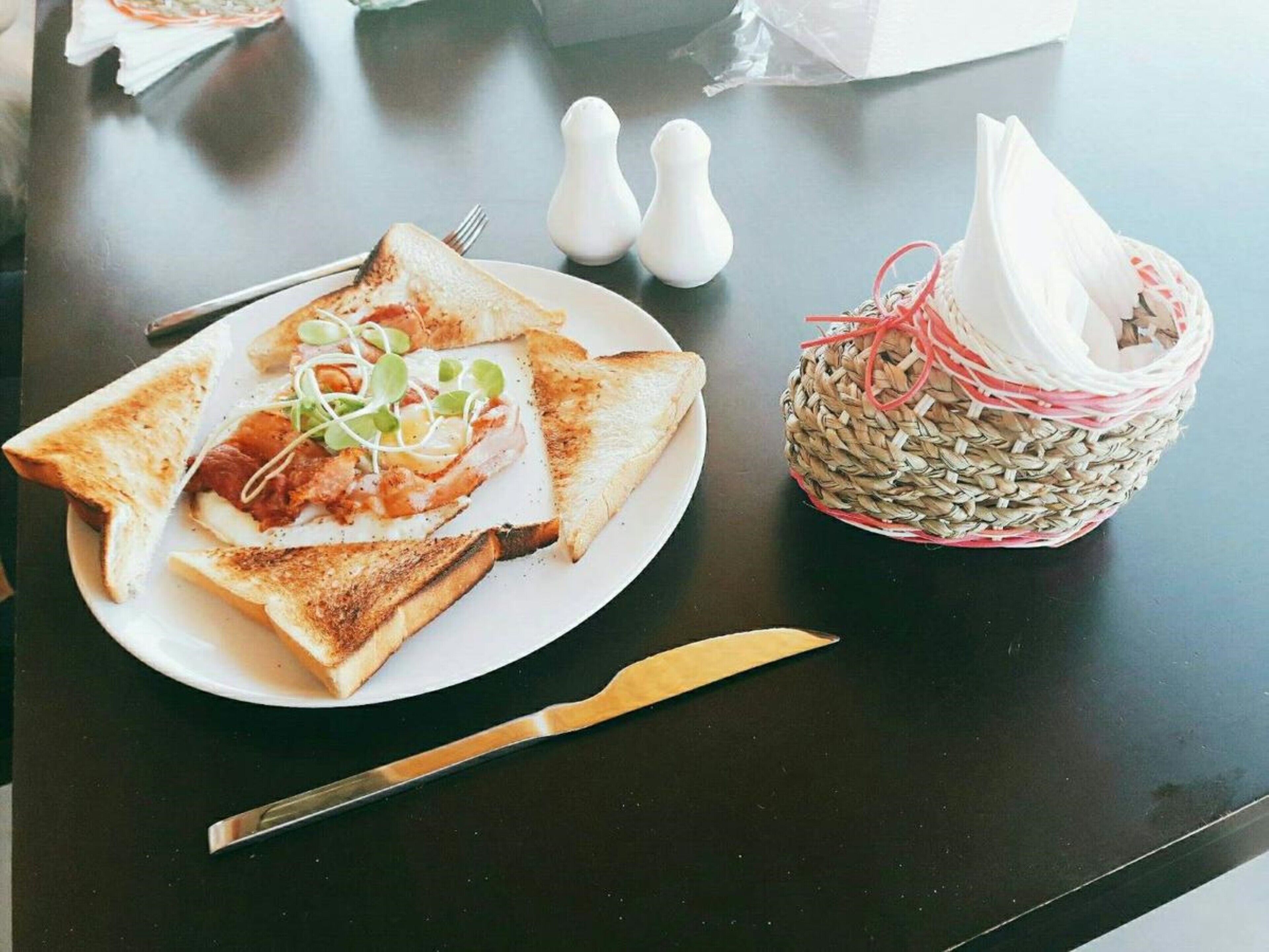 Un plato con pan tostado, un sándwich y una cesta tejida con una servilleta.