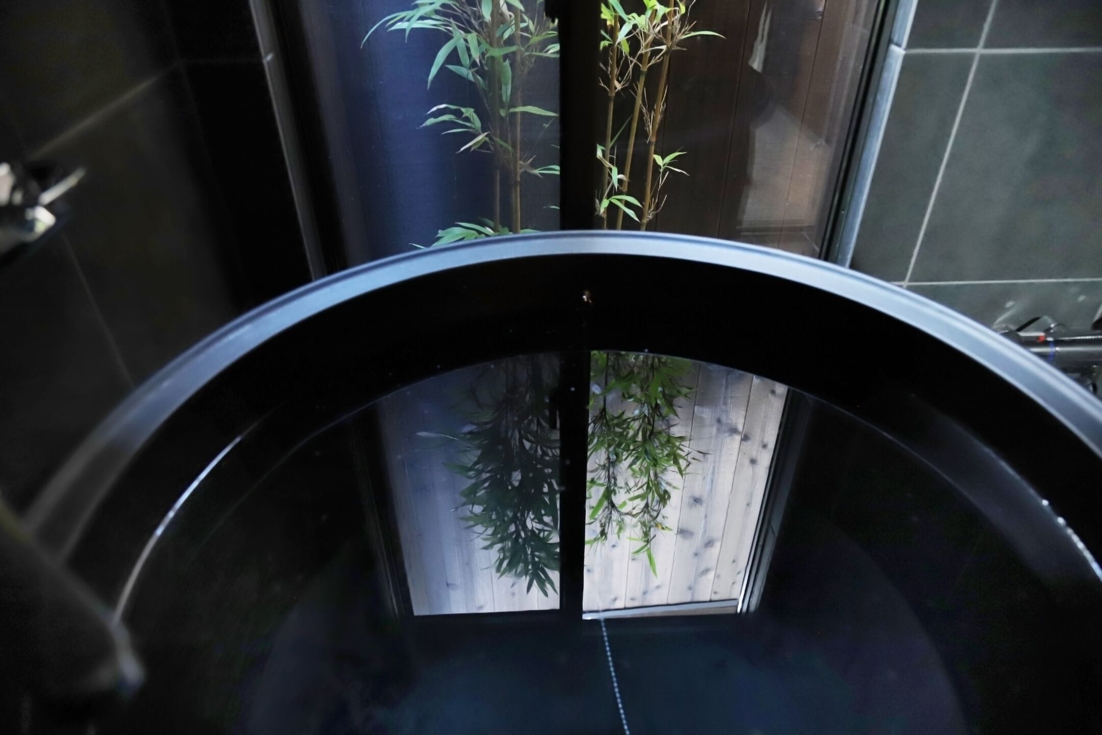 A bathroom with a black bathtub, a wooden floor, and bamboo plants.