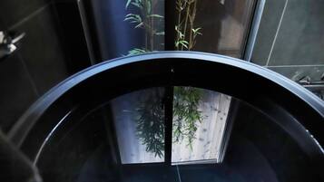 A bathroom with a black bathtub, a wooden floor, and bamboo plants.