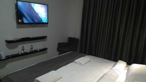 Une chambre d’hôtel avec un lit, un téléviseur fixé au mur, une chaise et une fenêtre avec des rideaux.