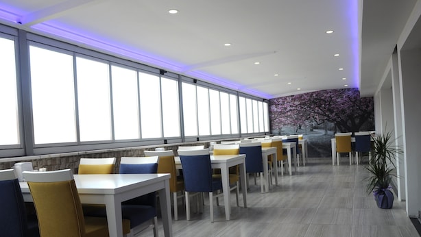Un espace de restauration moderne avec des tables et des chaises blanches, de grandes fenêtres et une fresque murale.
