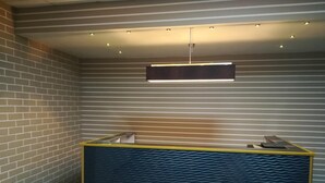 Un comptoir d’accueil doté d’un plateau bleu texturé et d’un bord jaune, placé devant un mur à rayures, avec un luminaire horizontal au-dessus.