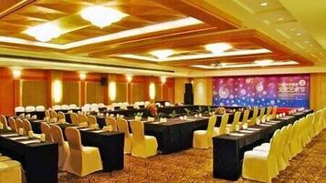 A conference room with rows of tables and chairs, a stage with a backdrop, and a patterned carpet.