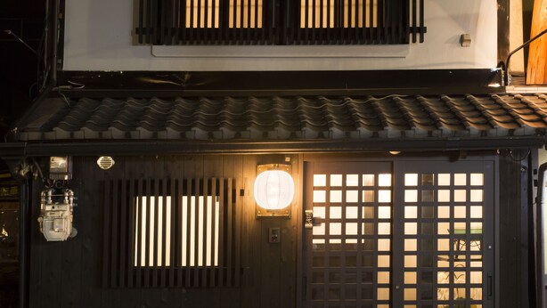 Ein traditionelles japanisches Gebäude mit einer dunklen Holztür, einem Laternen und einem Ziegeldach.