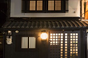 A traditional Japanese building with a dark wooden door, a lantern, and a tiled roof. - Kyomachiya Gion KANAU (Kyoto)