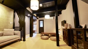 Ein Wohnzimmer mit einer Couch, einer Holzbank, Tatami-Matten und einem traditionellen japanischen Schrank.