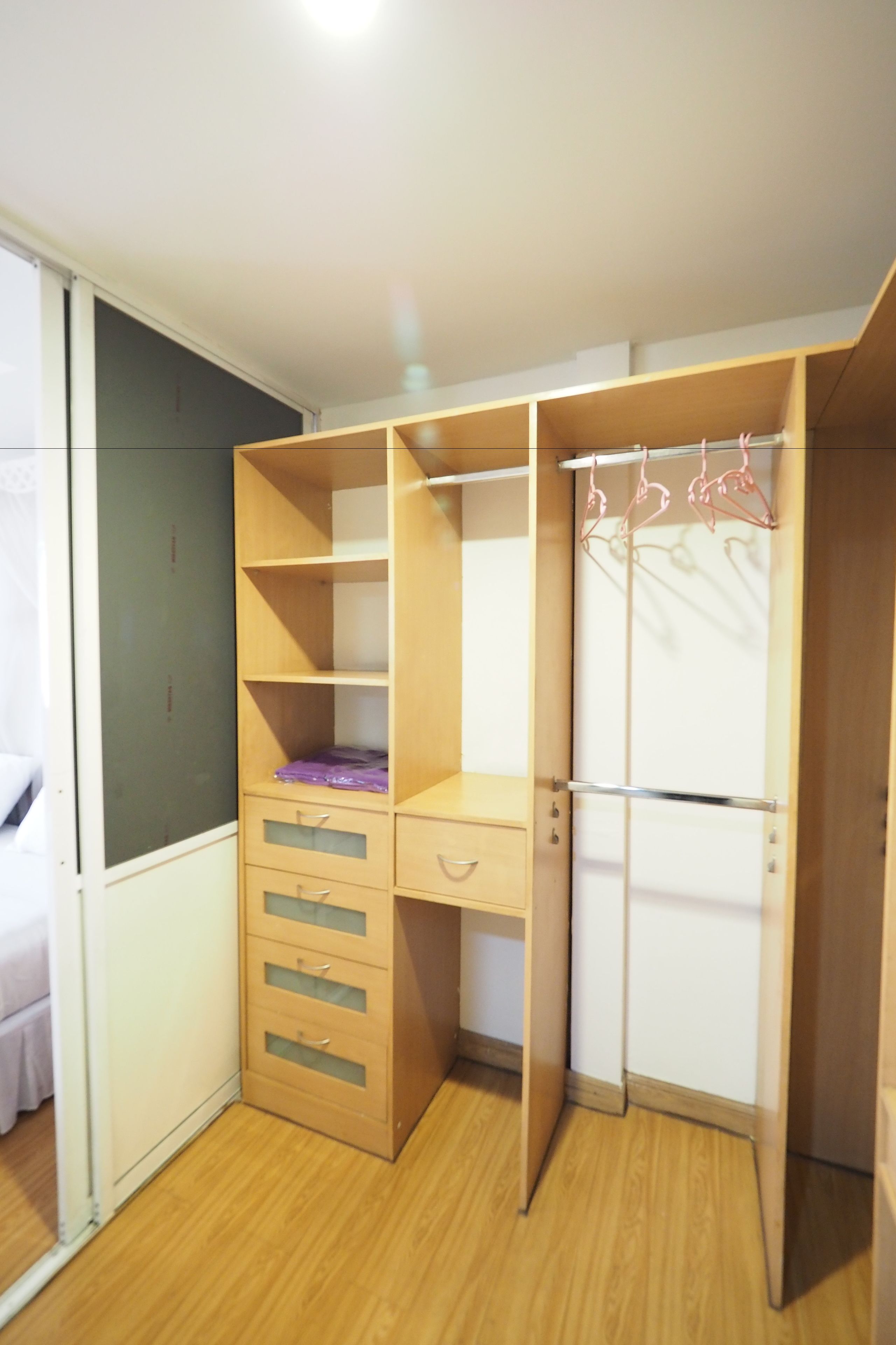 A room with a wooden wardrobe, a bed, and a mirror.