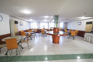A spacious dining area with multiple tables and chairs, a central round table, and a clock on the wall.