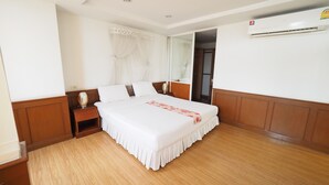 A hotel room with a large bed, wooden flooring, a nightstand, and an air conditioning unit. - Navanakorn Golden View (Khlong Luang)