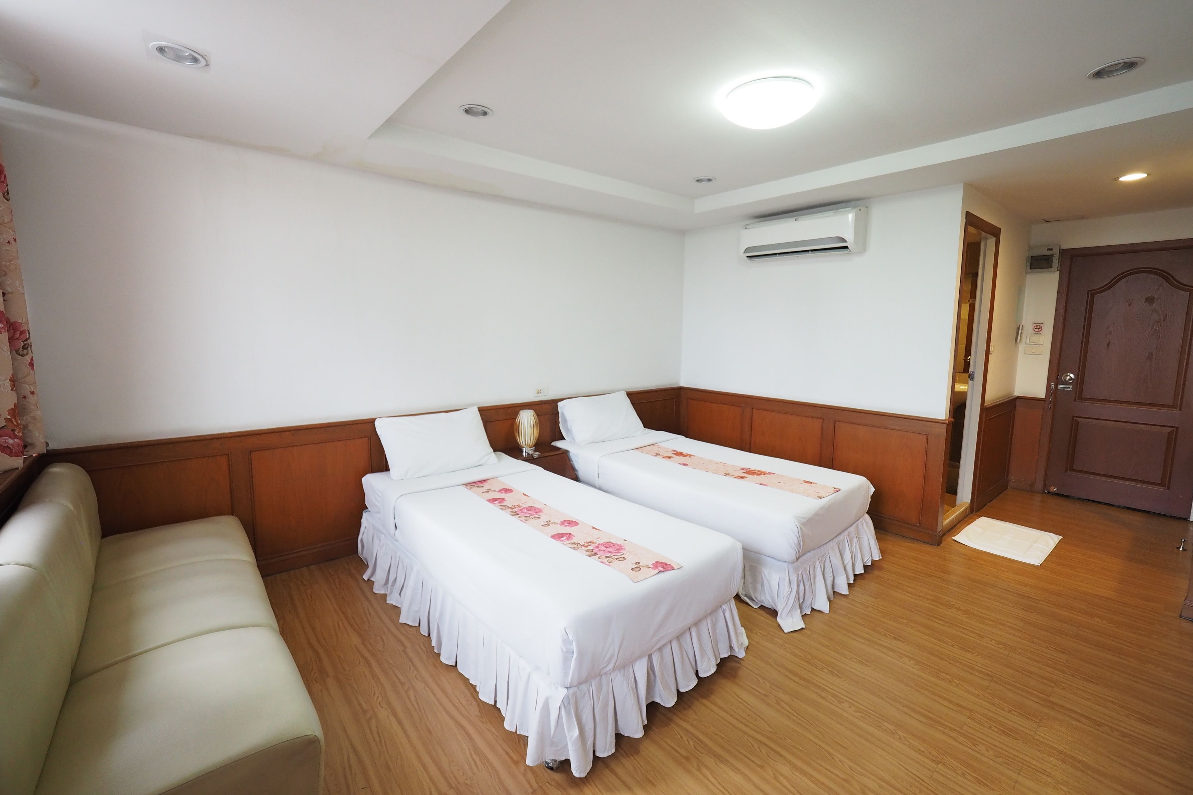 Una habitación de hotel con dos camas individuales, un banco de madera y un equipo de aire acondicionado en la pared.