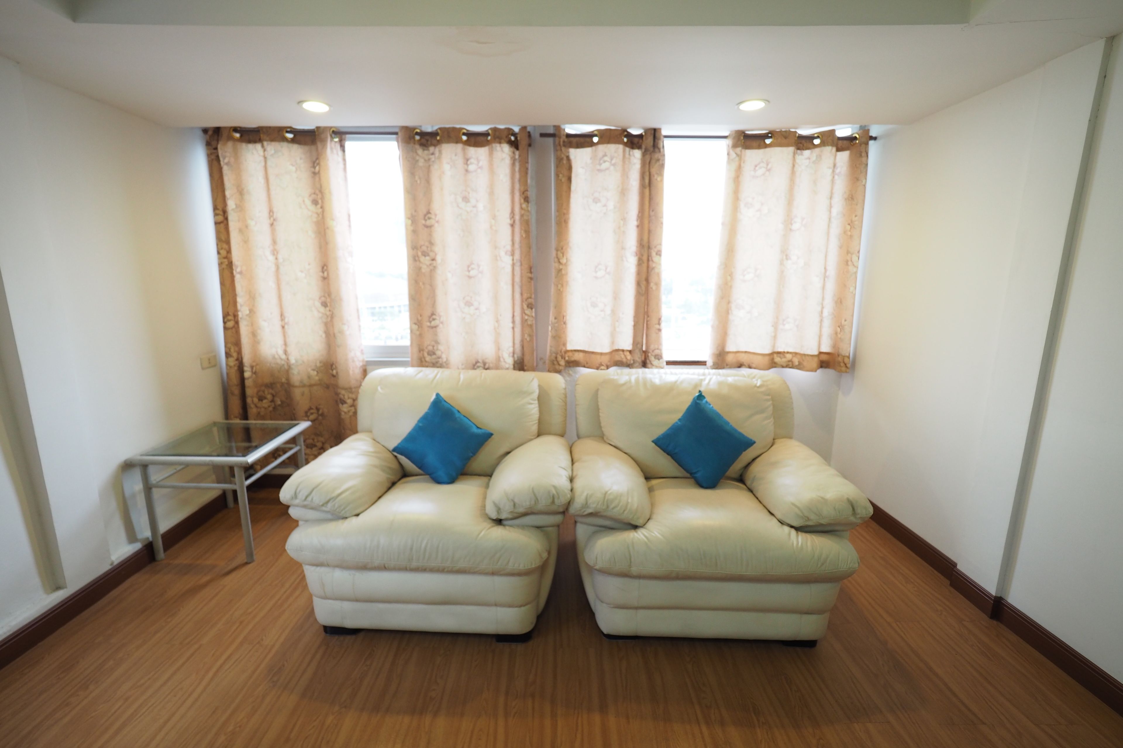 A room with two beige leather armchairs with blue cushions, a small glass table, and a window with patterned curtains.