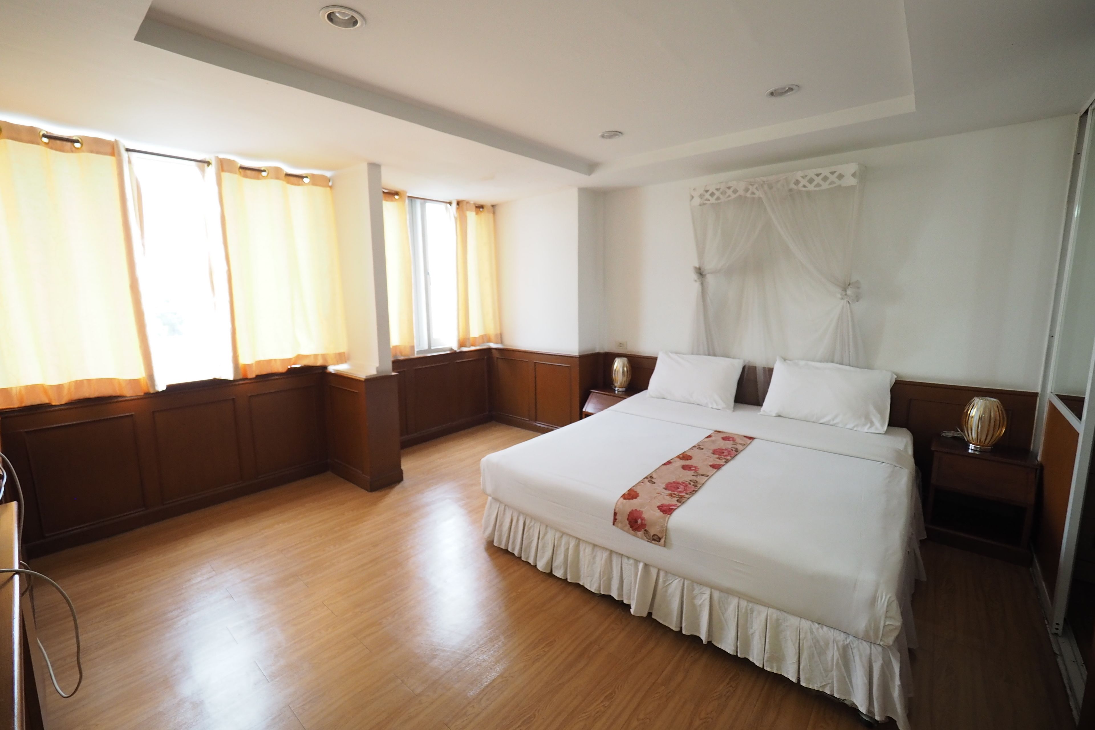 A hotel room with a large bed, wooden flooring, and a view of the outdoors through the windows.