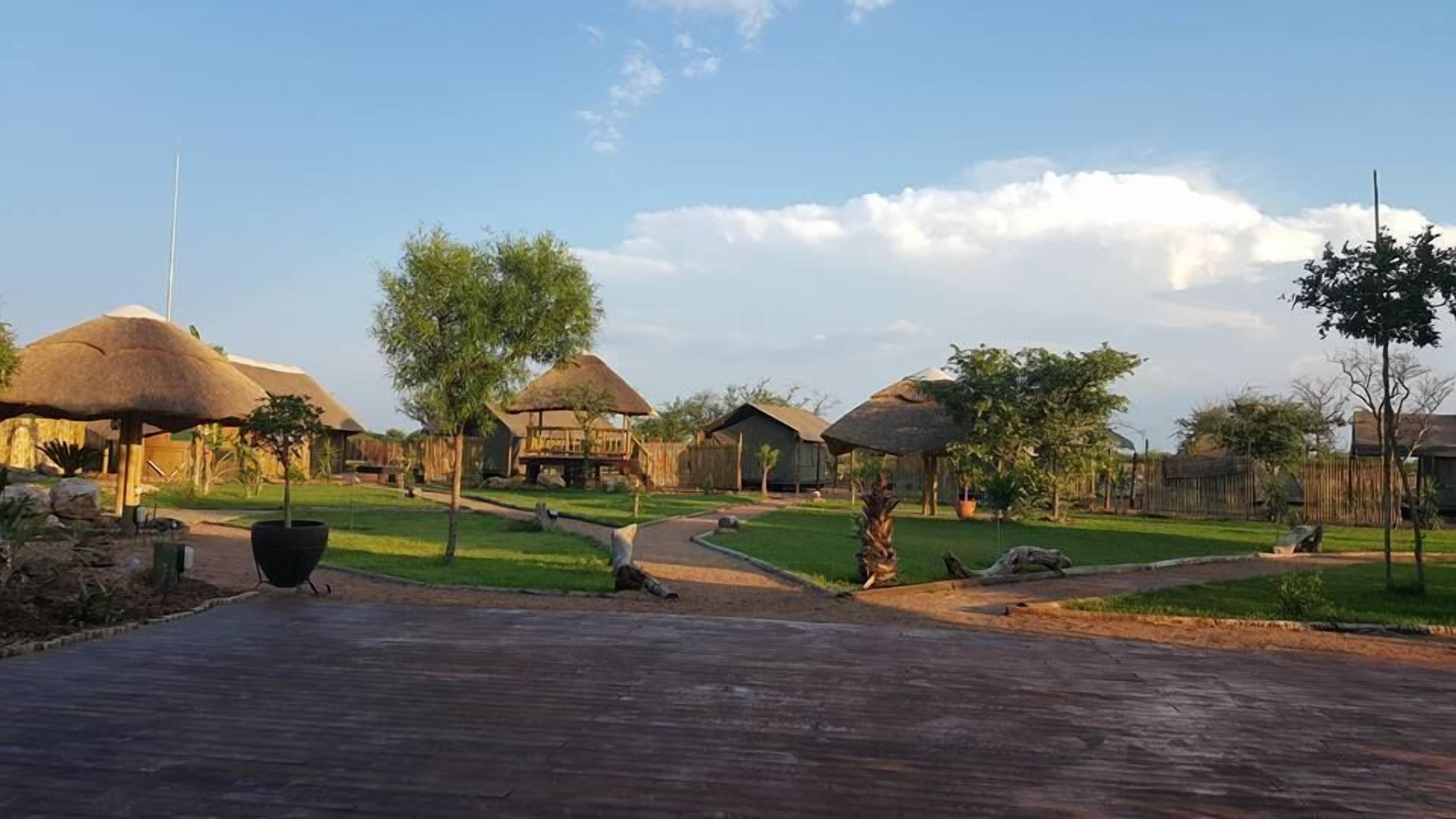 A resort with thatched-roof huts, a paved walkway, and a grassy area with trees.